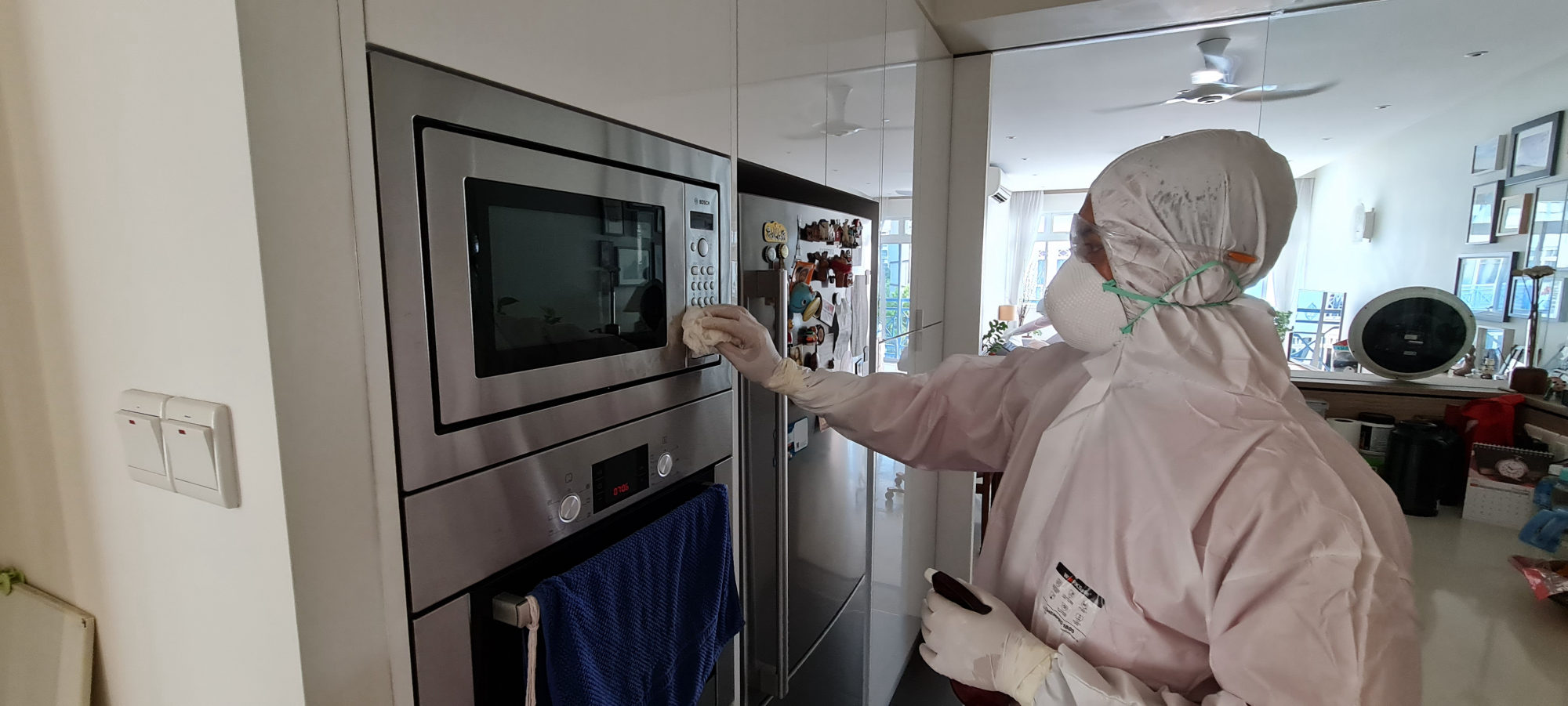 Technician in PPE applying disinfection treatment to a surface in a clinical interior